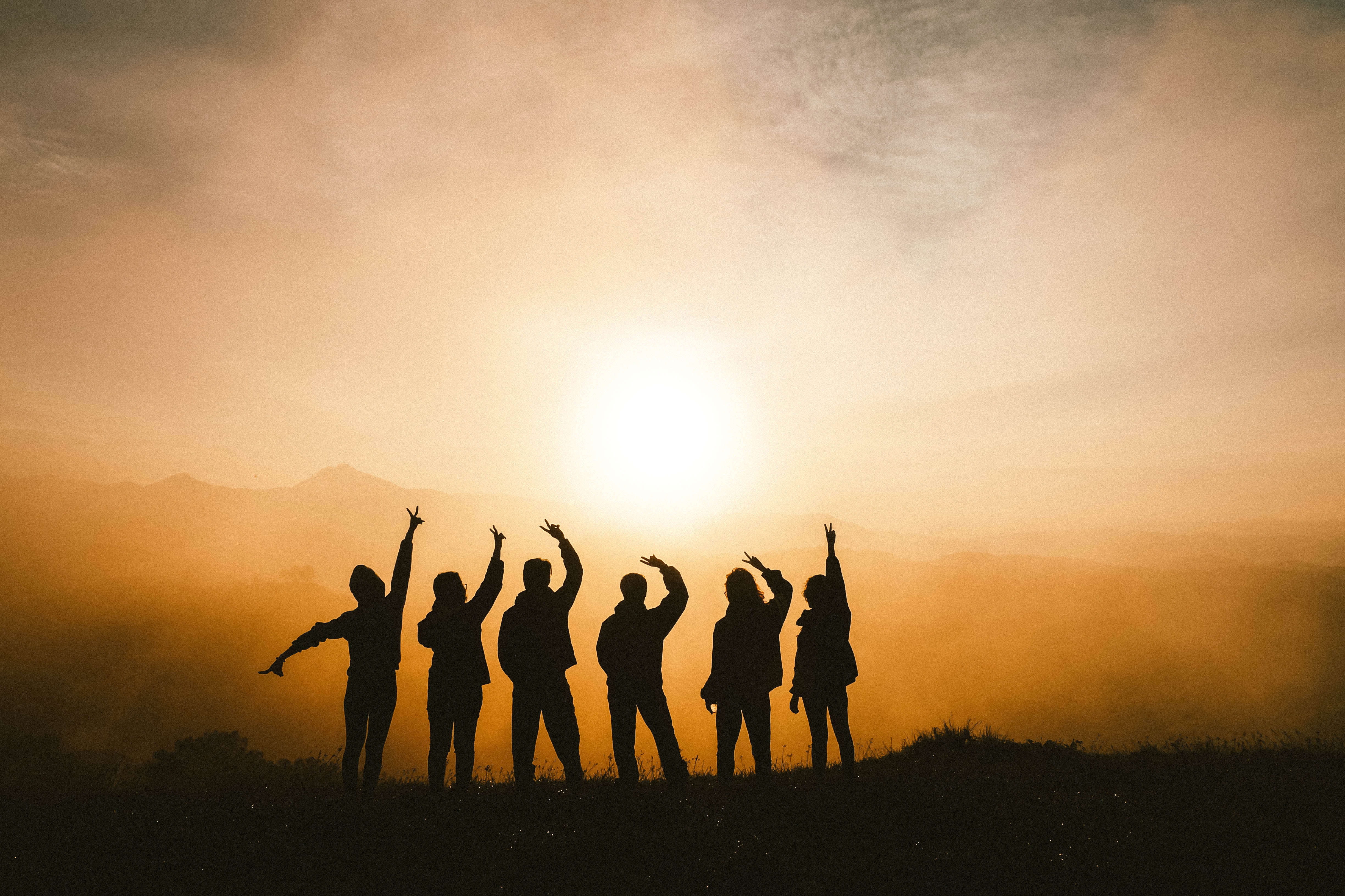 6 people in silhouette pointing at the sun rising in the sky.